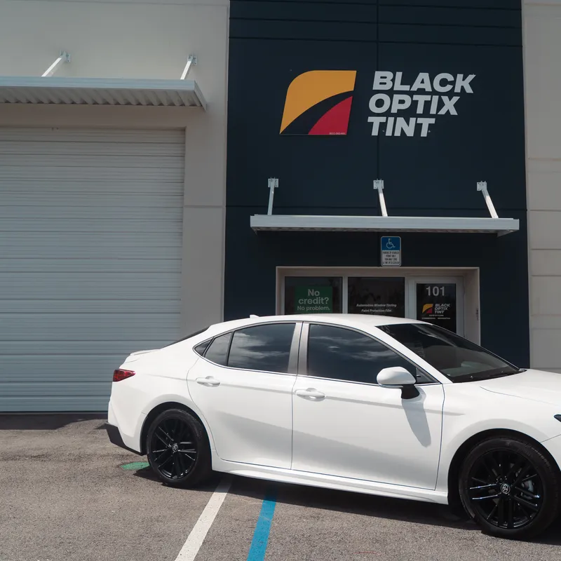 White Toyota Camry with new window tint under the Black Optix Tint sign