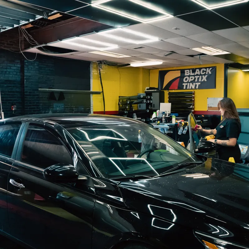 Black sedan with freshly tinted windows inside a Black Optix Tint bay