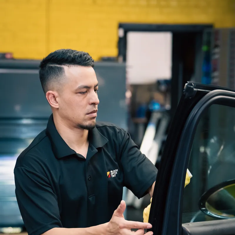 Technician installing window tint on door glass in a Black Optix Tint bay