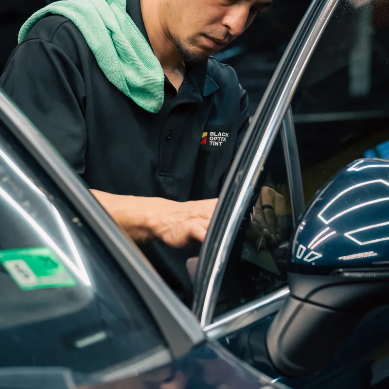 Black Optix Tint technician fitting window film on a Porsche door