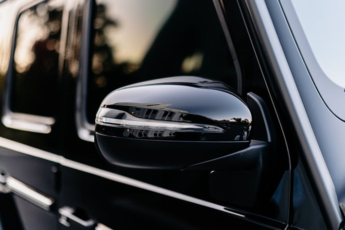 Close-up of glossy black side mirror and dark window tint on a luxury SUV, highlighting professional automotive tint work by Black Optix Tint.