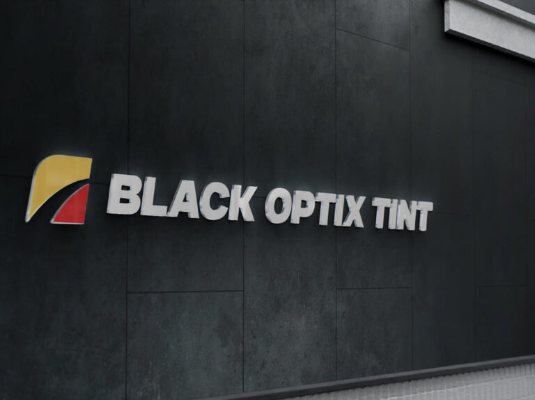 Sign on a dark wall displaying the name "Black Optix Tint" with a yellow and red logo to the left of the text.