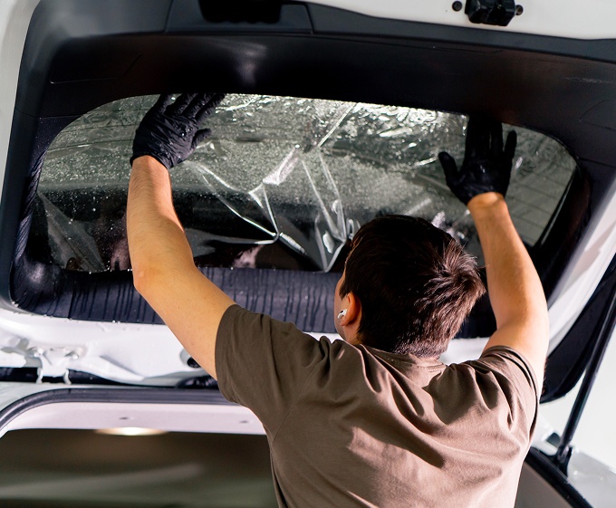 Installer applying clear protective film to a vehicle rear window for added safety and shatter resistance at Black Optix Tint.