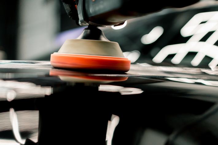 A close-up of a polishing machine buffing the surface of a black car, creating a shiny reflection.