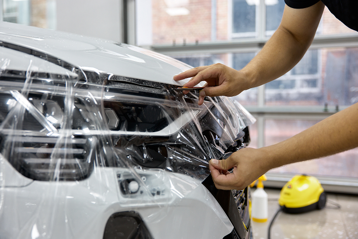 Technician applying clear paint protection film (PPF) to a vehicle headlight for chip and scratch protection at Black Optix Tint.